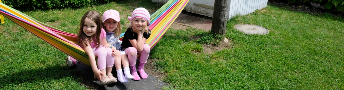Drei kleine Mädchen sitzen in einer Hängematte.